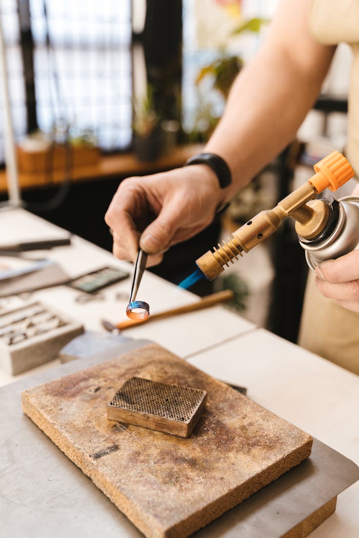 Close-up of a jeweler using a torch to shape a silver ring in a studio workshop.